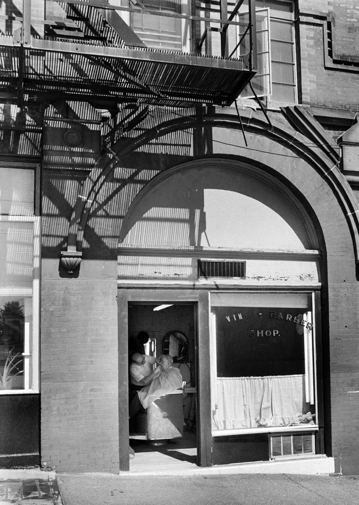 Vinnie Iovino Sr., owner of Vin's Barbershop in downtown Danbury, takes care of customers early on a Saturday morning. 1980.