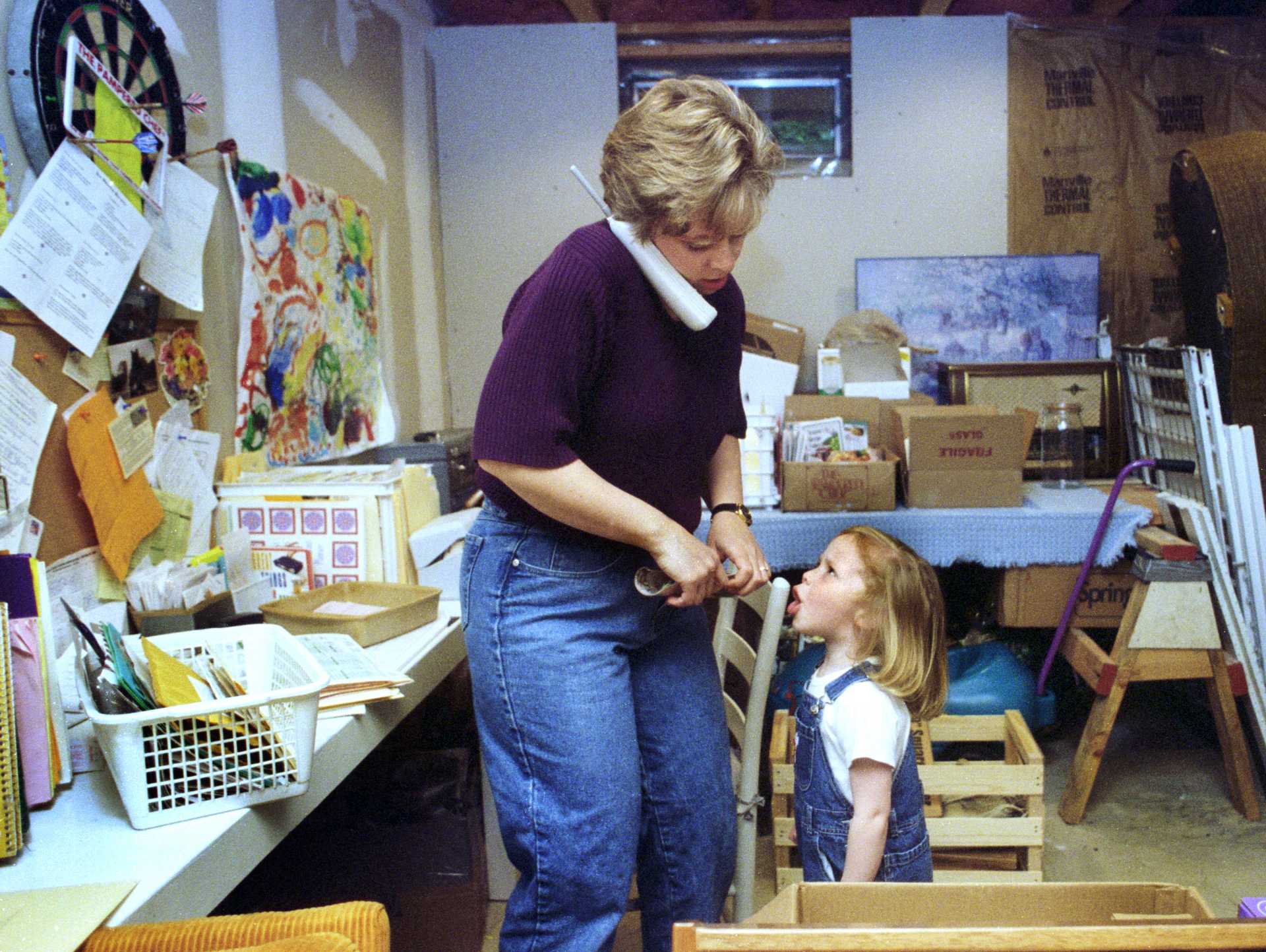 A mother takes a business call and listens to her daughter vent at the same time. Photo taken as part of a Mother's Day story on mothers that work from home.